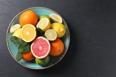 Photo of Different cut and whole citrus fruits on black table, top view. Space for text