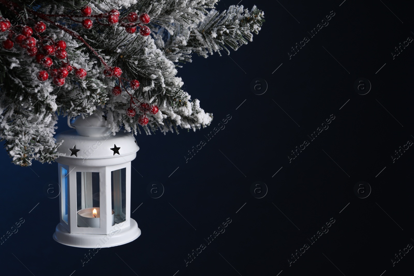 Photo of Christmas lantern with burning candle on fir tree against dark background, closeup. Space for text