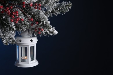 Christmas lantern with burning candle on fir tree against dark background, closeup. Space for text