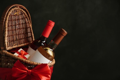 Photo of Festive basket with bottles of wine and gift against dark background. Space for text