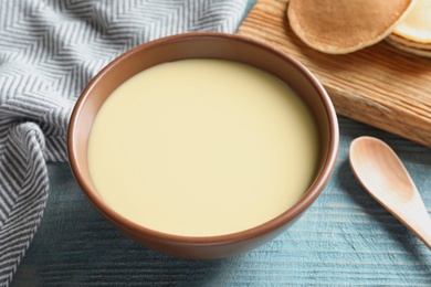 Photo of Bowl with condensed milk served on wooden table. Dairy products