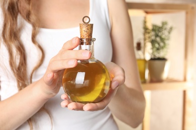 Young woman holding bottle of fresh olive oil, closeup