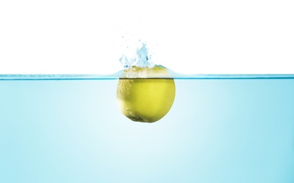 Photo of Green apple falling down into clear water against white background