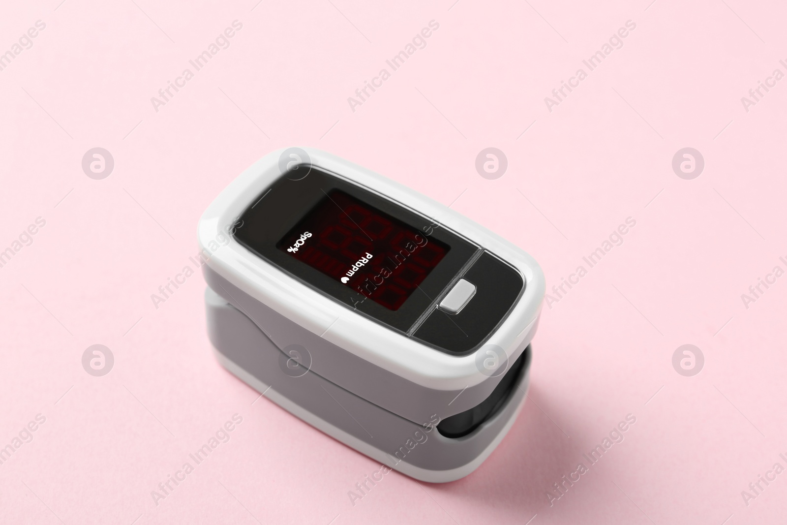 Photo of Modern fingertip pulse oximeter on pink background, closeup