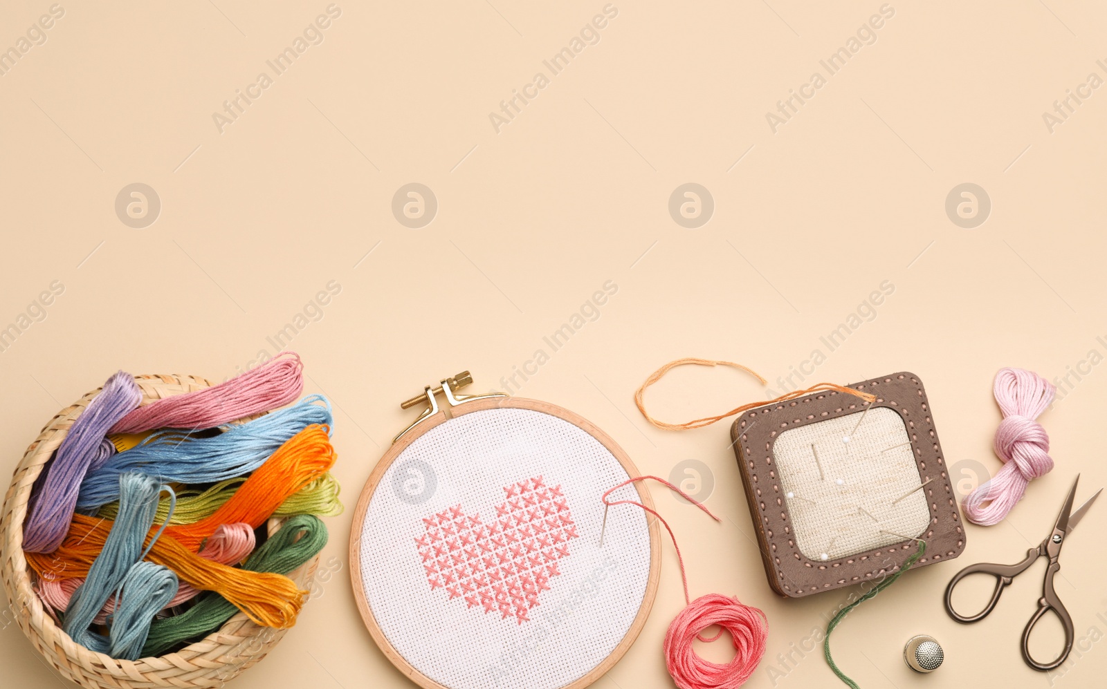 Photo of Flat lay composition with embroidery and different sewing accessories on beige background. Space for text