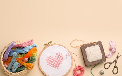 Flat lay composition with embroidery and different sewing accessories on beige background. Space for text