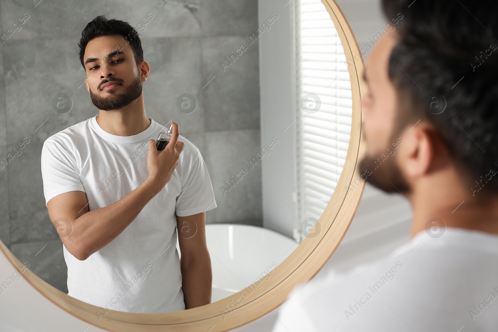 Photo of Man spraying luxury perfume near mirror indoors