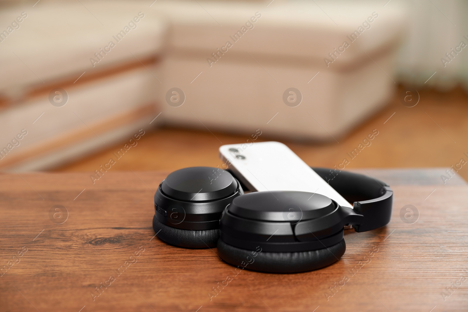 Photo of Modern wireless headphones and smartphone on wooden table indoors