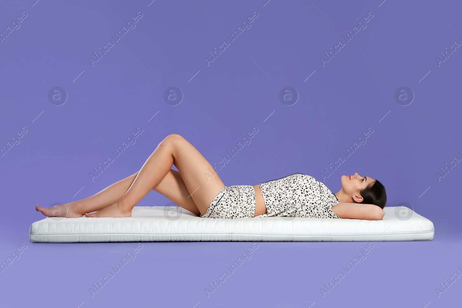 Photo of Young woman lying on soft mattress against light purple background