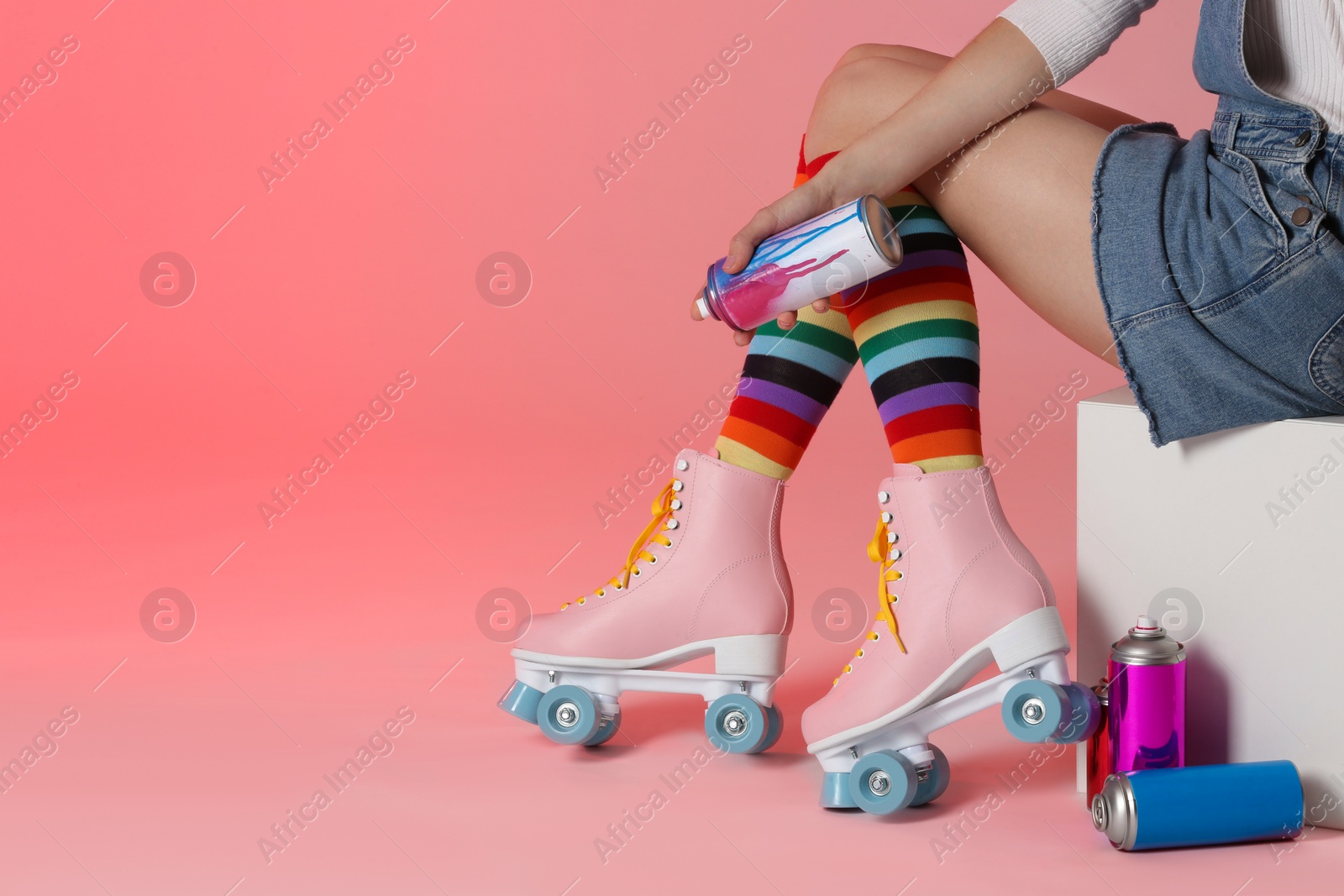 Photo of Woman with vintage roller skates and spray paint cans on color background, closeup. Space for text