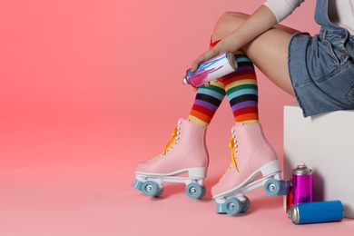 Photo of Woman with vintage roller skates and spray paint cans on color background, closeup. Space for text