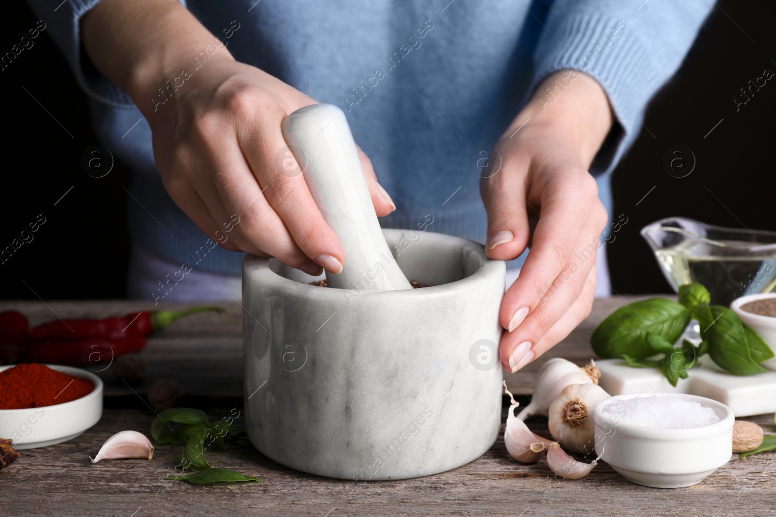 Photo of Woman grinding coriander at wooden table, closeup