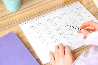 Photo of Woman with calendar at wooden table in office, closeup
