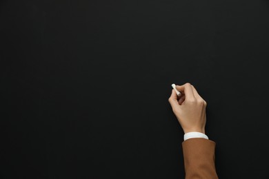 Woman with white chalk near blackboard, closeup. Space for text