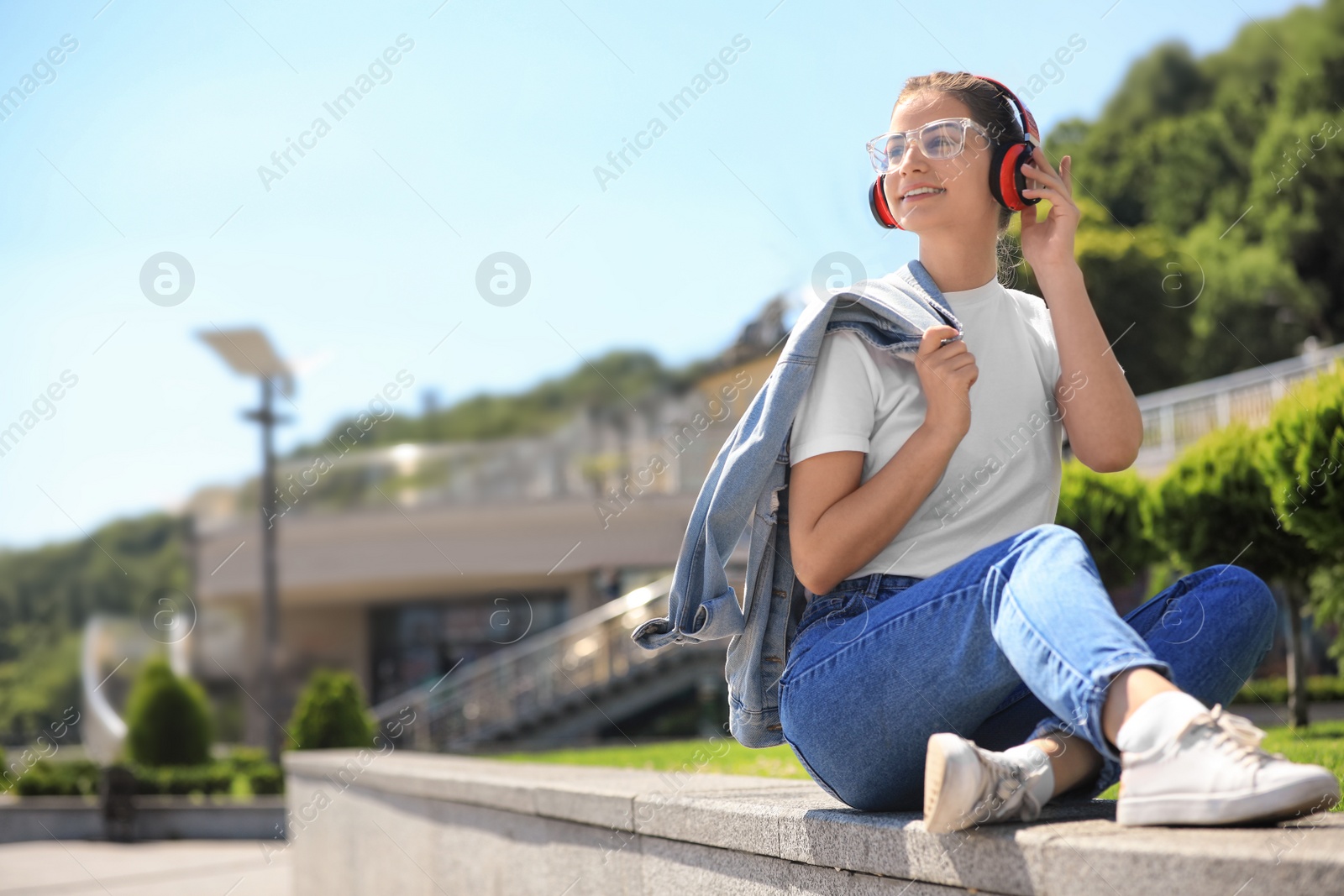 Photo of Young woman with headphones listening to music on city street. Space for text