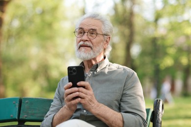 Photo of Portrait of happy grandpa with glasses using smartphone on bench in park