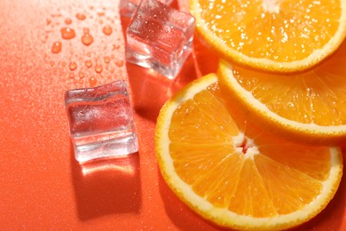 Photo of Slices of juicy orange and ice cubes on terracotta background, closeup