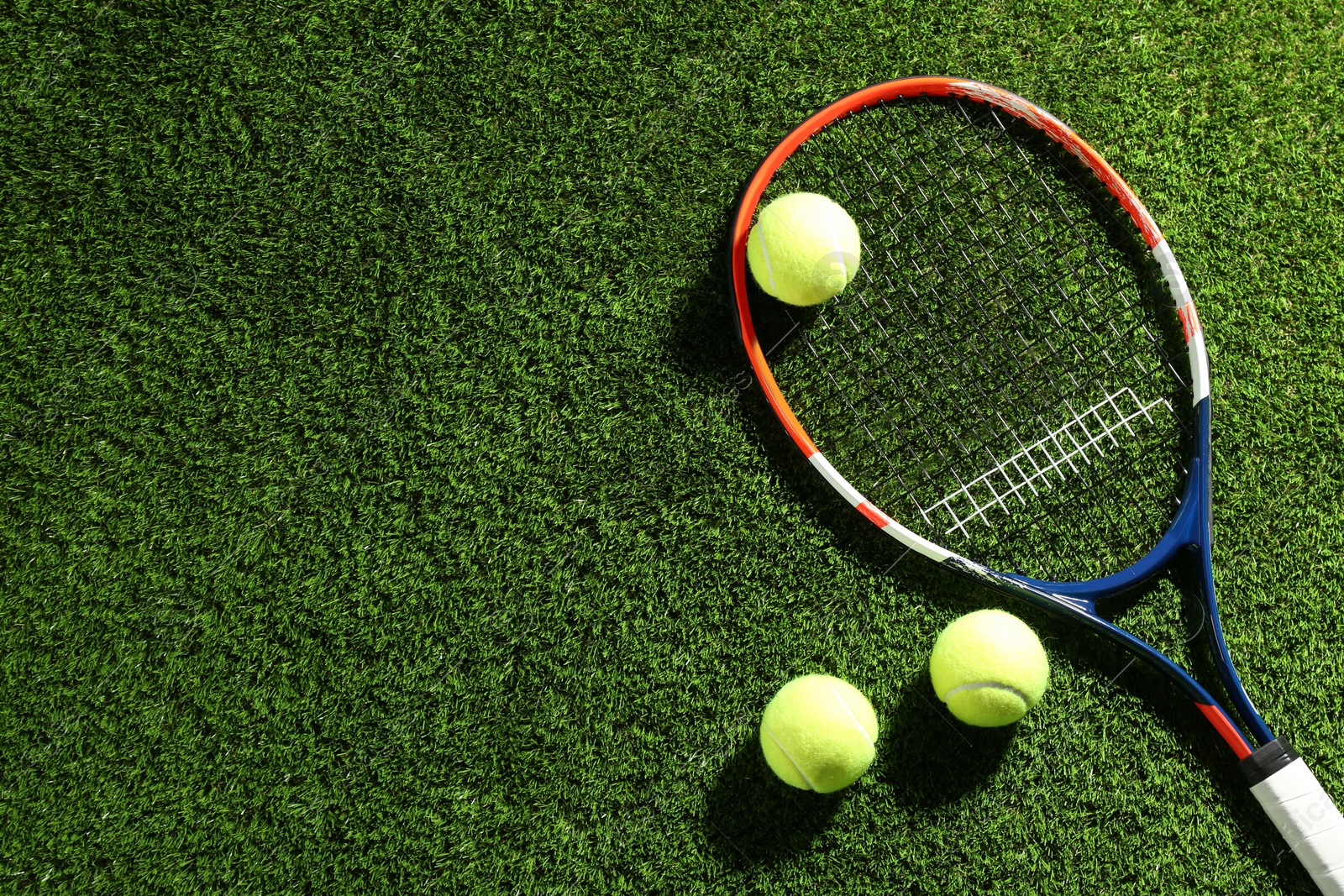 Photo of Tennis racket and balls on green grass, flat lay. Space for text