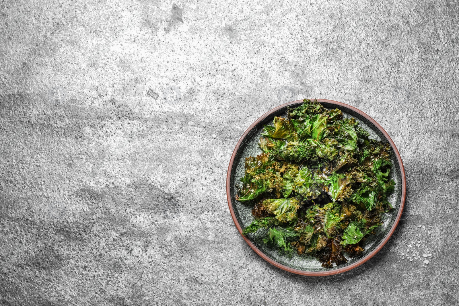 Photo of Tasty baked kale chips on grey table, top view. Space for text