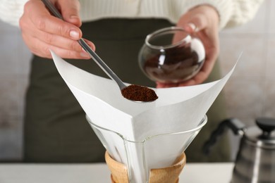Making drip coffee. Woman adding ground coffee into chemex coffeemaker with paper filter, closeup