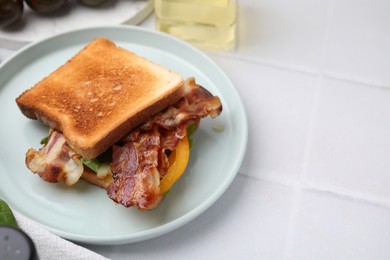 Tasty sandwich with bacon and bell pepper on white tiled table, space for text