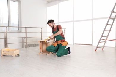 Carpenter in uniform making furniture indoors. Professional construction tools