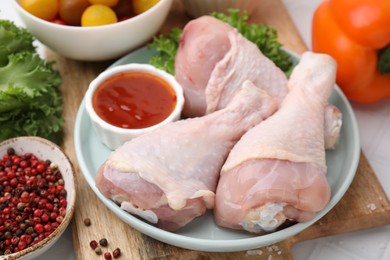 Photo of Fresh marinade, raw chicken drumsticks and other products on table, closeup