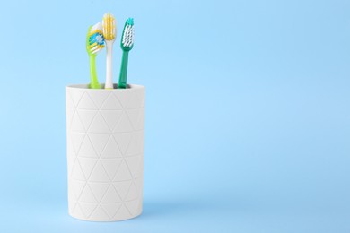 Photo of Different toothbrushes in holder on light blue background. Space for text