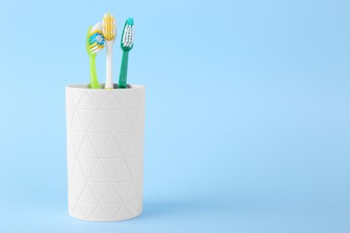 Different toothbrushes in holder on light blue background. Space for text