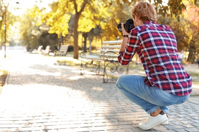 Photo of Young male photographer taking photo with professional camera in park. Space for text