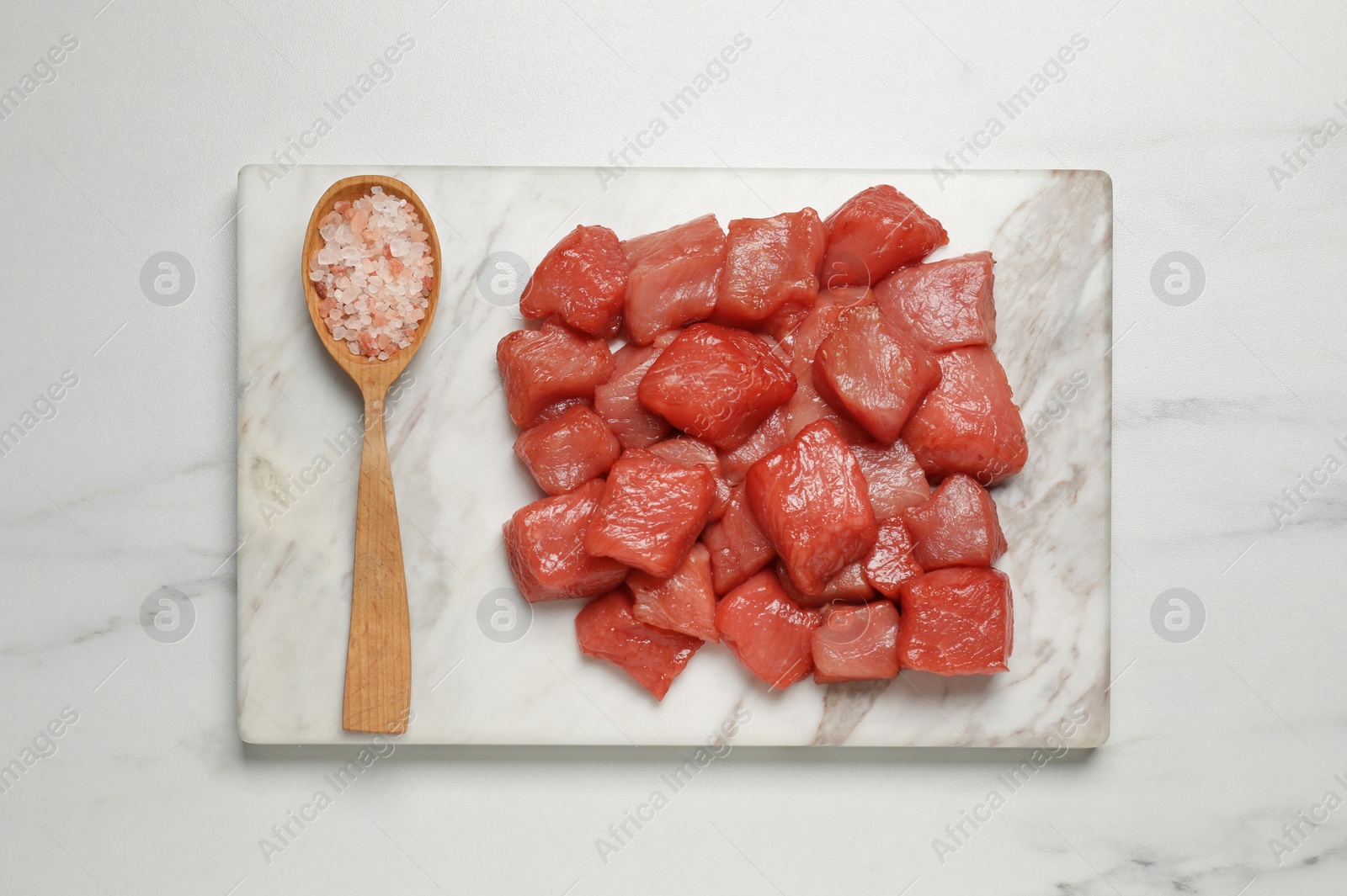 Photo of Cooking delicious goulash. Raw beef meat and sea salt on white marble table, top view