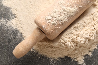 Photo of Scattered flour and rolling pin on grey textured table, top view