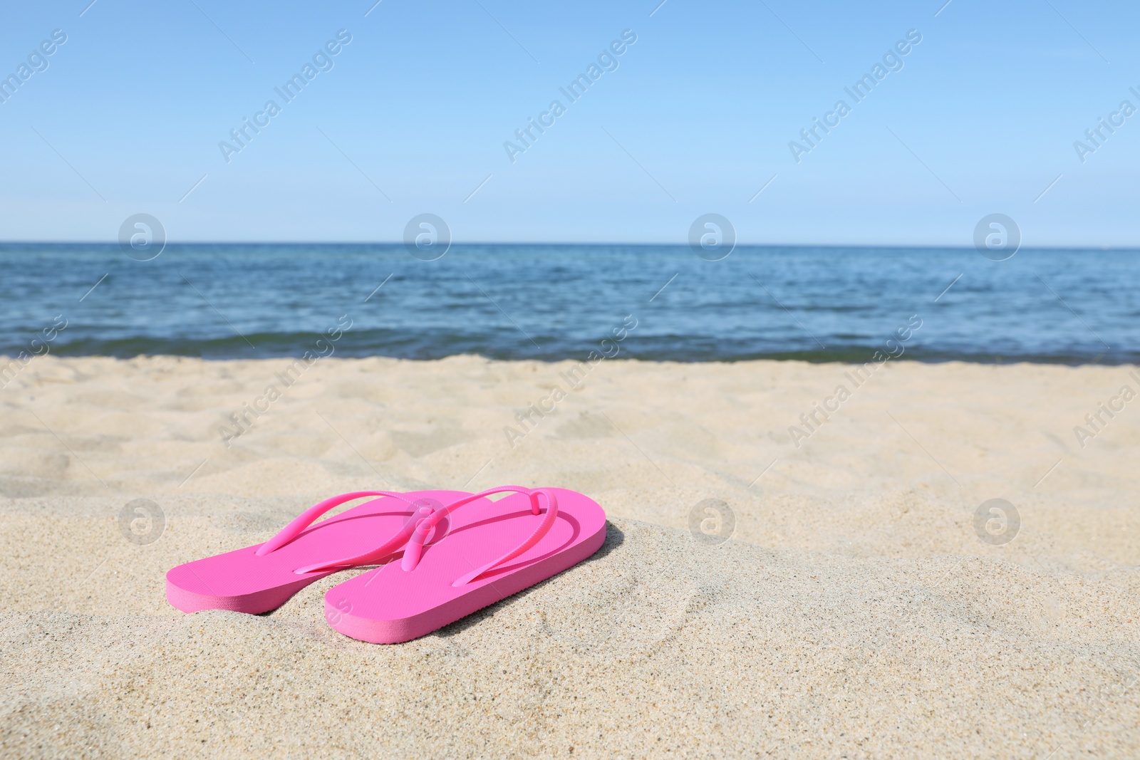 Photo of Stylish pink flip flops on beach sand, space for text