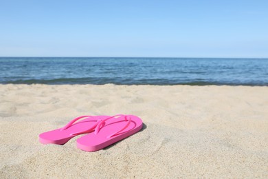 Photo of Stylish pink flip flops on beach sand, space for text