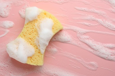 Yellow sponge with foam on pink background, top view