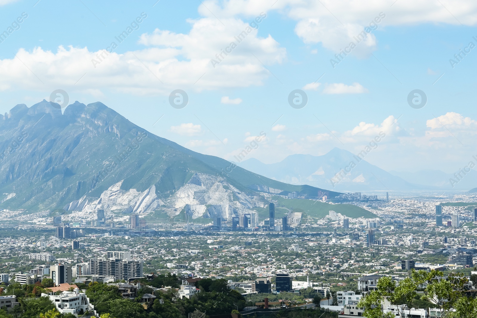 Photo of Picturesque view of trees, buildings and mountains under beautiful sky in city