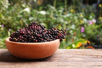 Photo of Bowl with tasty elderberries (Sambucus) on wooden table outdoors, space for text