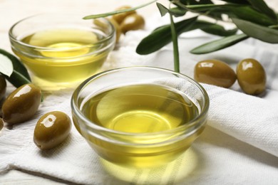 Photo of Bowls with cooking oil and olives on white wooden table, closeup