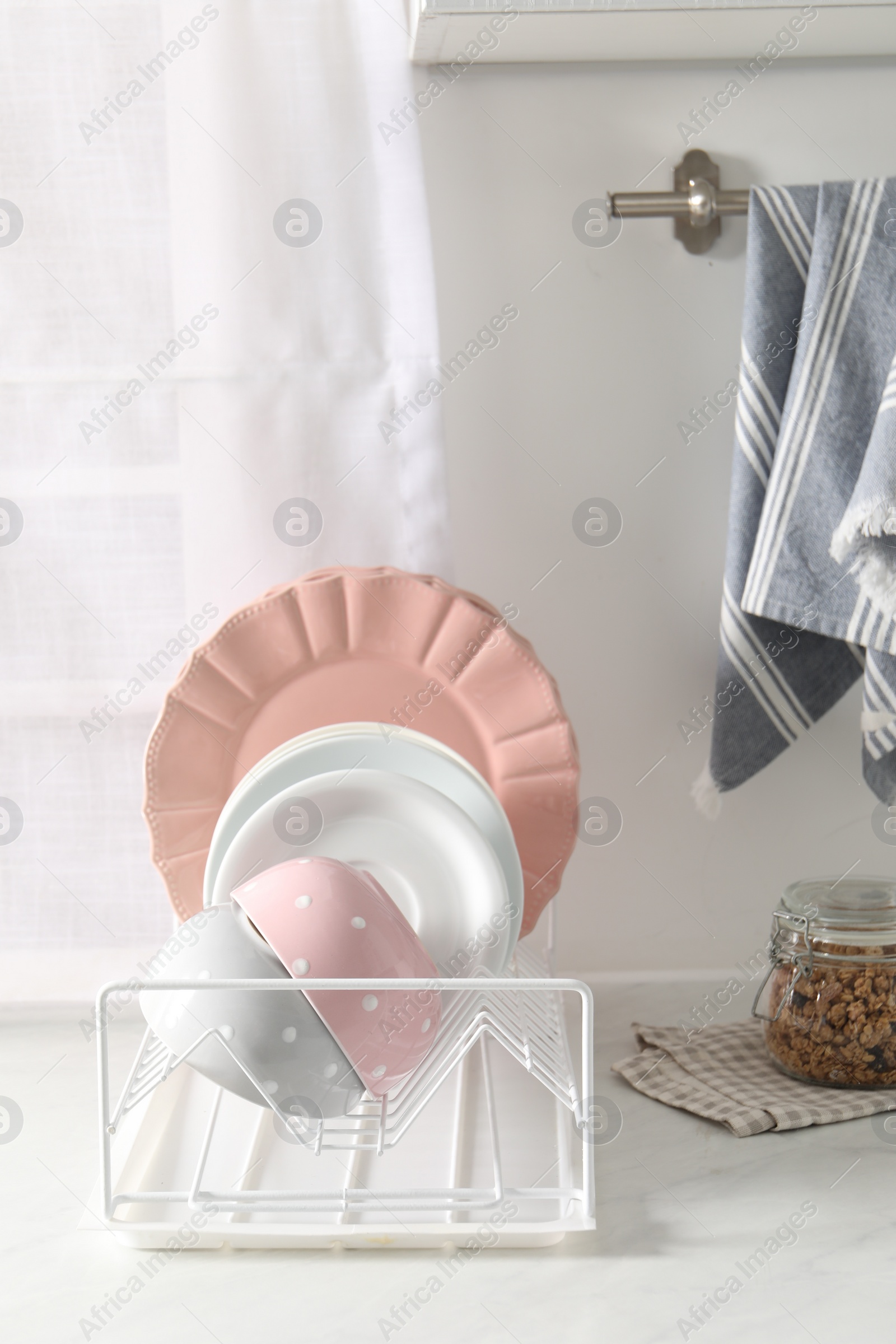 Photo of Drainer with different clean dishware on white table in kitchen