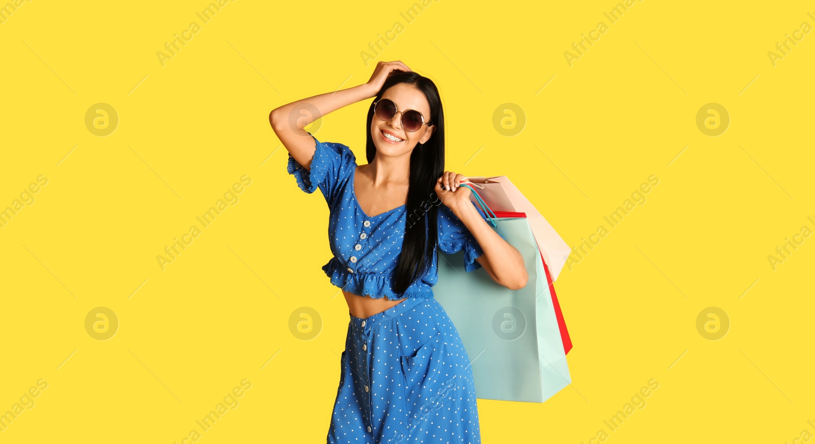 Photo of Beautiful young woman with paper shopping bags on yellow background