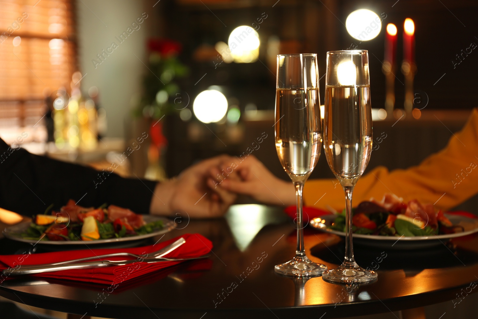 Photo of Couple having romantic dinner in restaurant, closeup. Focus on glasses of champagne