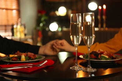 Photo of Couple having romantic dinner in restaurant, closeup. Focus on glasses of champagne