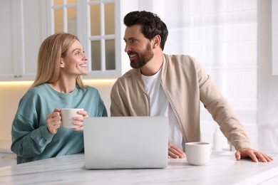 Happy couple with laptop at white table in kitchen