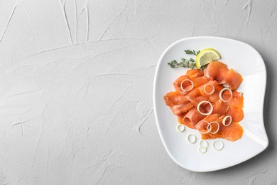 Plate with fresh sliced salmon fillet and onion on light background, top view