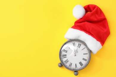 Photo of Alarm clock and Santa hat on yellow background, top view with space for text. New Year countdown