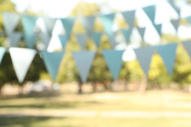 Photo of Blurred view of light blue bunting flags in park. Party decor