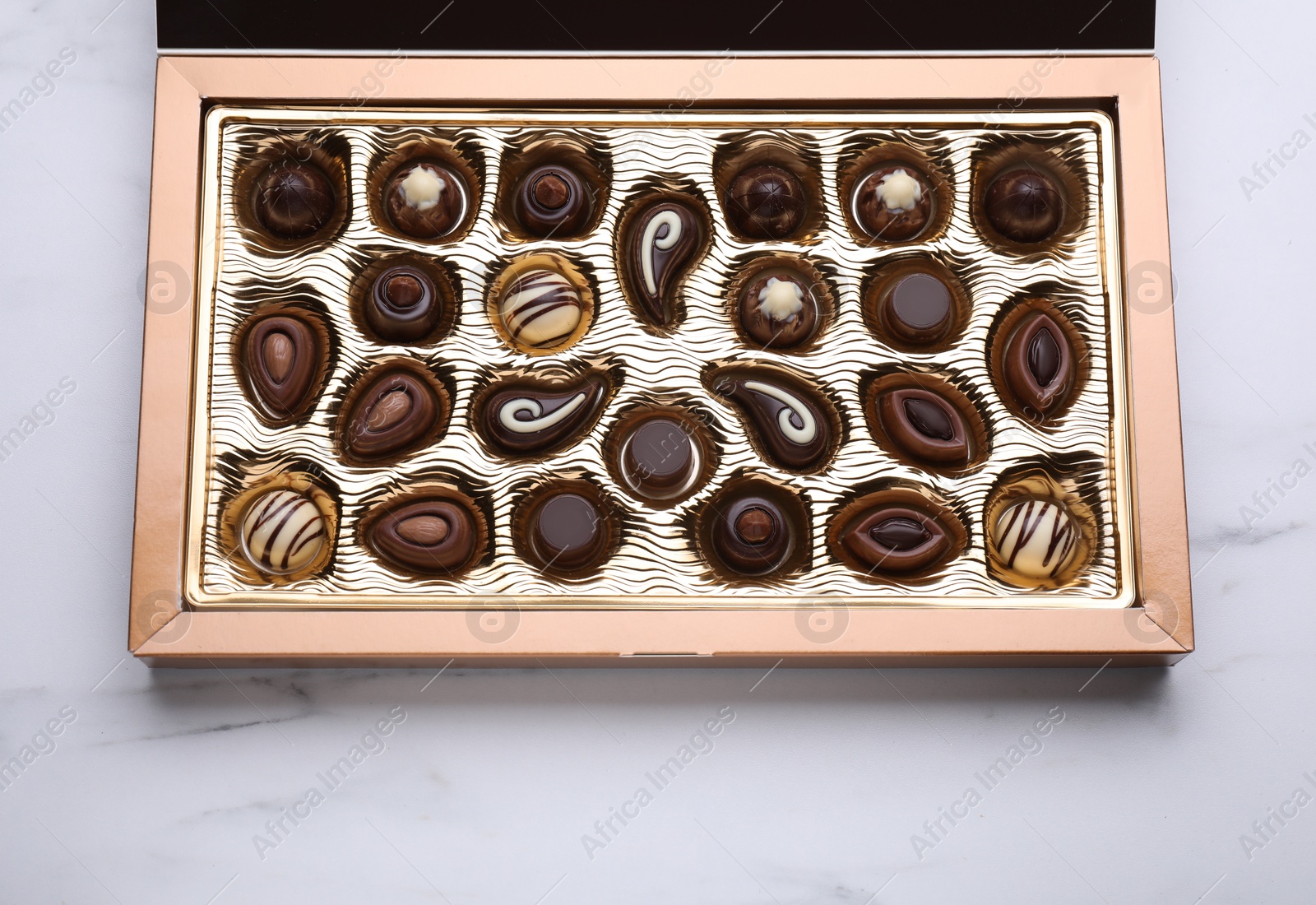 Photo of Box of delicious chocolate candies on white marble table, top view