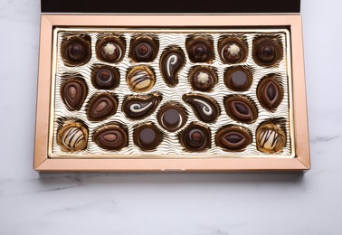 Box of delicious chocolate candies on white marble table, top view