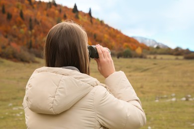 Woman looking through binoculars in beautiful mountains, back view