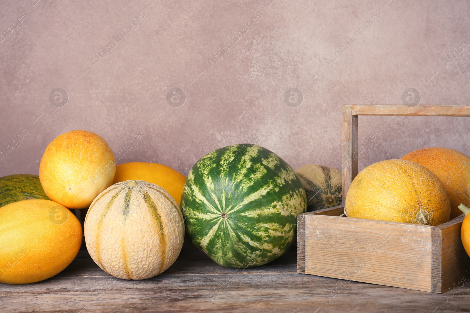 Photo of Ripe melons and watermelon on wooden table against color background. Space for text